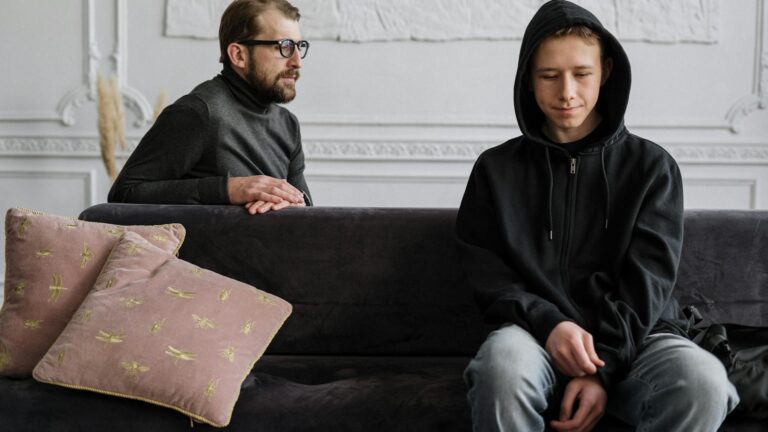 Therapist sits behind man on couch.