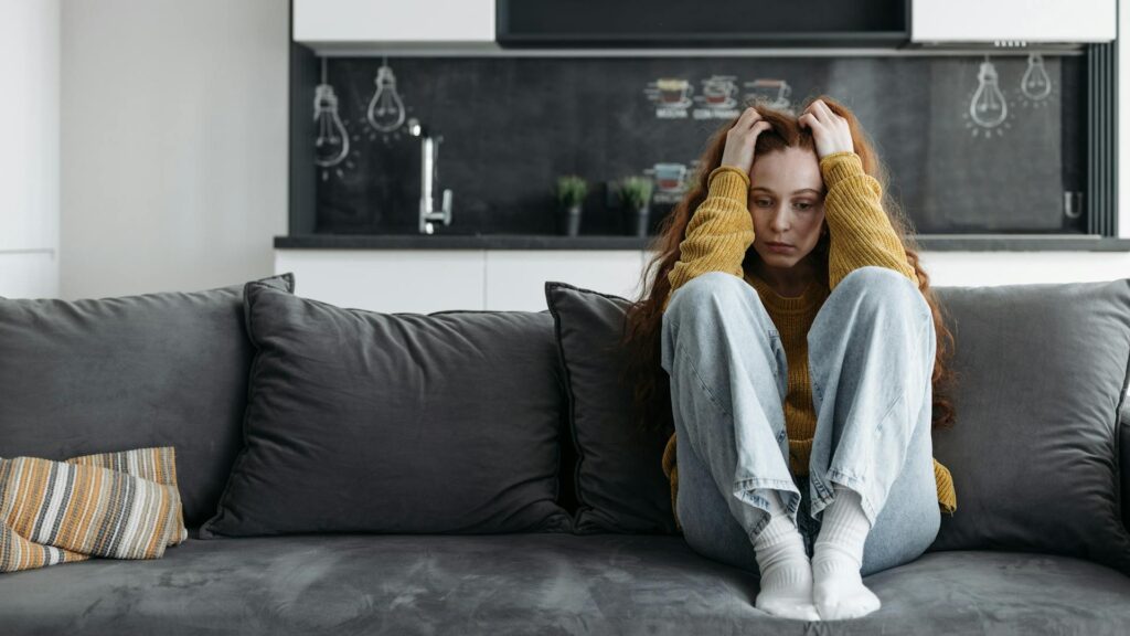 Woman sits on a couch, upset.